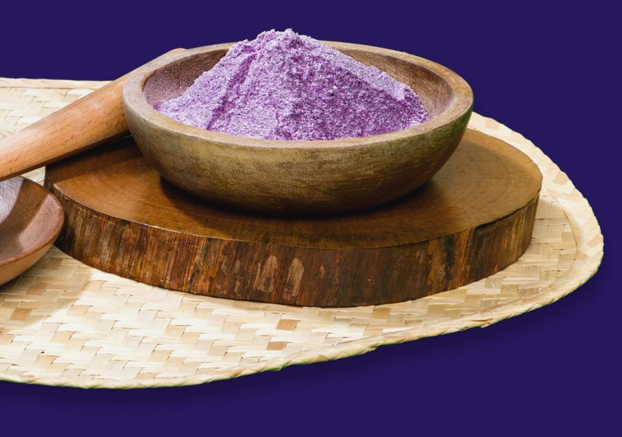 A wooden bowl heaped with fine purple ube powder on a woven mat
