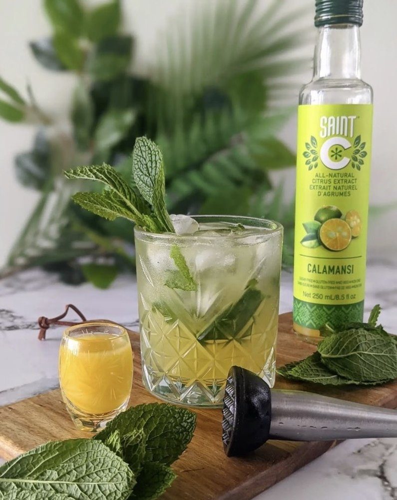 A calamansi and mint cooler beside a bottle of Saint C Calamansi