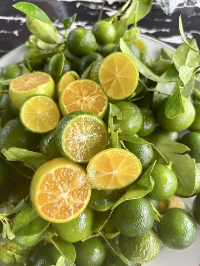 Halved calamansi limes piled on a plate with leaves